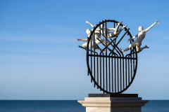 Flight of the Langoustine, by Pierre Diamantopoulo MRSS. It is made of four life-size bronze figures flying through a steel grid. It was inspired by a discarded and mangled lobster pot that the artist had found on Brighton beach. In his imagination, the washed-up object that had seemingly helped the lobsters escape, translated itself into a wider story of human exodus and release – a dash for freedom. Diamantopoulo describes the figures as “at once profound, frivolous and boisterous, occupying the air like a flock of birds and inspired by modern dance choreography”. Bronze casting at Milwyn Foundry and fabrication of the steel grid and assembly by Art Fabrications. The sculpture weighs 2.2 tonnes and measures approximately 3.5 metres high and 3 meters wide. Flight of the Langoustine was inaugurated on the Hove Plinth on 17 September 2023. Flight of the Langoustine, by Pierre Diamantopoulo MRSS. It is made of four life-size bronze figures flying through a steel grid. It was inspired by a discarded and mangled lobster pot that the artist had found on Brighton beach. In his imagination, the washed-up object that had seemingly helped the lobsters escape, translated itself into a wider story of human exodus and release – a dash for freedom. Diamantopoulo describes the figures as “at once profound, frivolous and boisterous, occupying the air like a flock of birds and inspired by modern dance choreography”. Bronze casting at Milwyn Foundry and fabrication of the steel grid and assembly by Art Fabrications. The sculpture weighs 2.2 tonnes and measures approximately 3.5 metres high and 3 meters wide. Flight of the Langoustine was inaugurated on the Hove Plinth on 17 September 2023.
